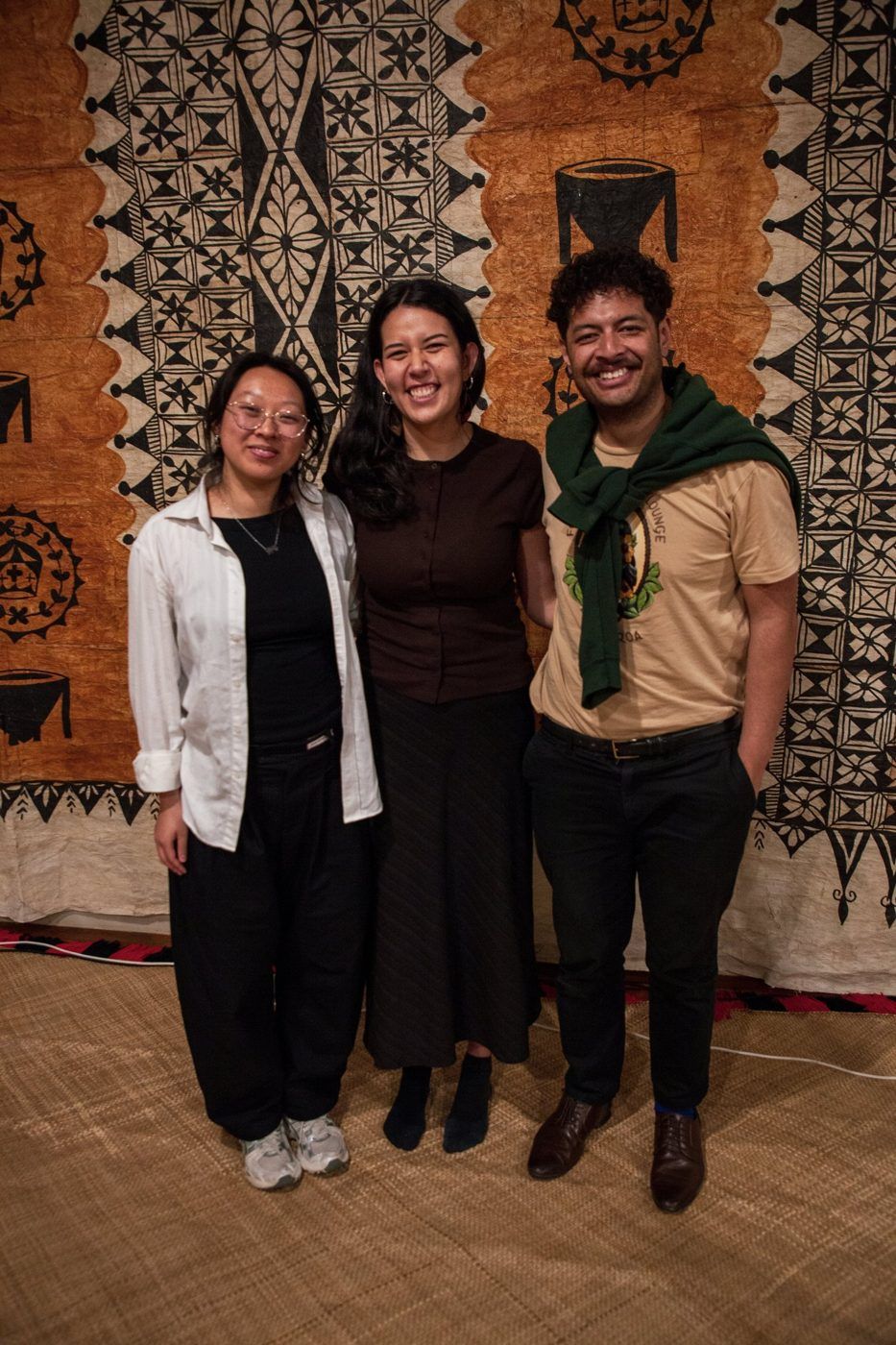 Three members of the Te Kāhui team in front of a ngatu.